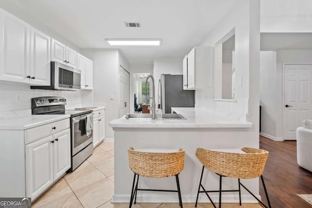 1825 Millstone Ct, Alpharetta, GA 30004 - kitchen featuring appliances with stainless steel finishes, a kitchen breakfast bar, white cabinets, tasteful backsplash, and a peninsula