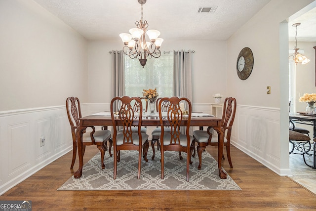 5086 N Woodbridge Trl, Stone Mountain, GA 30088 - dining space with a chandelier, wood finished floors, a decorative wall, wainscoting, and a textured ceiling