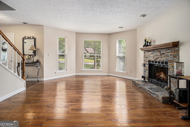 5086 N Woodbridge Trl, Stone Mountain, GA 30088 - unfurnished living room featuring wood-type flooring, plenty of natural light, a stone fireplace, a textured ceiling, and stairs