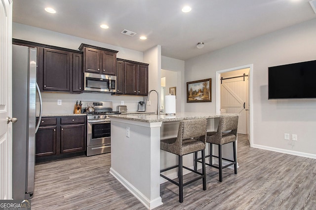111 Point View Dr, Canton, GA 30114 - kitchen with stainless steel appliances, light wood-style floors, an island with sink, a barn door, and dark brown cabinetry