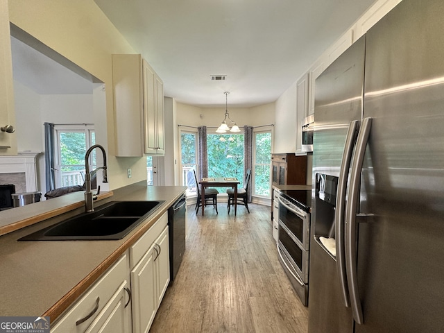 235 Pirkle Ct, Cumming, GA 30040 - kitchen featuring stainless steel appliances, light wood finished floors, decorative light fixtures, a fireplace, and a chandelier