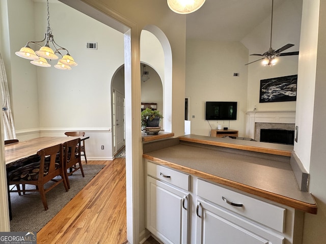 235 Pirkle Ct, Cumming, GA 30040 - kitchen featuring light wood-style floors, arched walkways, white cabinets, a fireplace, and a chandelier