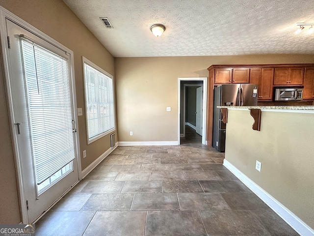 101 Riverchest Dr, Lagrange, GA 30240 - kitchen with appliances with stainless steel finishes, brown cabinetry, a breakfast bar area, a textured ceiling, and light stone counters