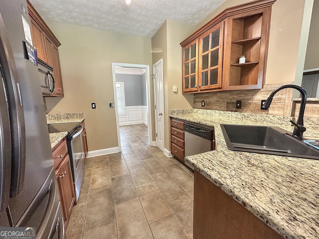 101 Riverchest Dr, Lagrange, GA 30240 - kitchen featuring appliances with stainless steel finishes, light stone counters, brown cabinetry, a textured ceiling, and a wainscoted wall