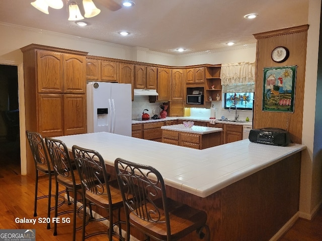 1904 S State Line Rd, Lagrange, GA 30240 - kitchen with white fridge with ice dispenser, under cabinet range hood, brown cabinetry, black electric stovetop, and ornamental molding