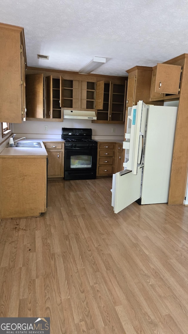 1448 SE Hillside Pl, Conyers, GA 30094 - kitchen with black range with gas stovetop, freestanding refrigerator, light wood finished floors, open shelves, and under cabinet range hood