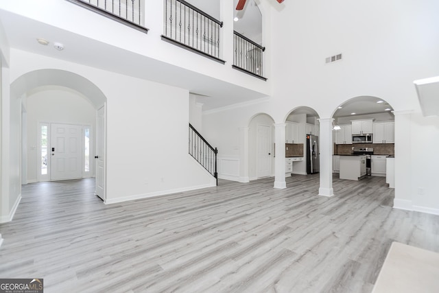 2023 Jameson Cir, Lawrenceville, GA 30043 - unfurnished living room featuring a towering ceiling, a ceiling fan, light wood-style floors, stairs, and ornate columns