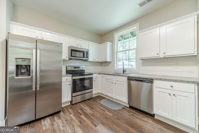 116 6th St, Monroe, GA 30655 - kitchen featuring appliances with stainless steel finishes, white cabinets, dark wood-style floors, and light stone counters