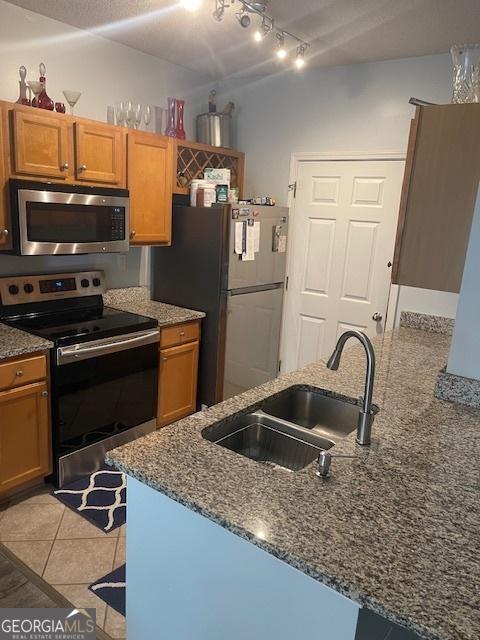 4333 Dunwoody Park Unit 2214, Atlanta, GA 30338 - kitchen with appliances with stainless steel finishes, dark stone counters, track lighting, a peninsula, and brown cabinetry