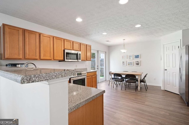 245 Weatherstone Pointe Dr, Woodstock, GA 30188 - kitchen featuring appliances with stainless steel finishes, brown cabinets, a peninsula, recessed lighting, and light wood-style floors