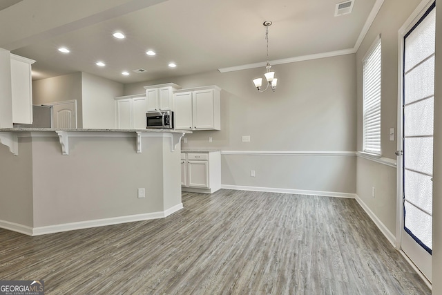 209 Merritt Cir, Newnan, GA 30263 - kitchen with stainless steel microwave, a breakfast bar area, white cabinetry, light wood-style floors, and a chandelier