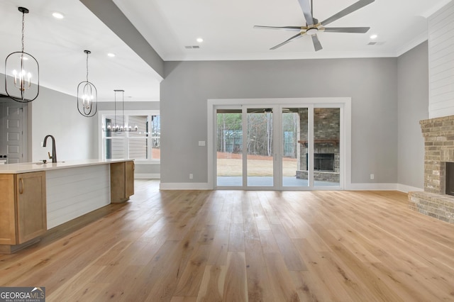 194 Forest Berry Ct Unit 98M2, Newnan, GA 30265 - unfurnished living room with a chandelier, a brick fireplace, crown molding, ceiling fan, and light wood-style flooring