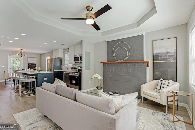 524 Paines Ave NW, Atlanta, GA 30318 - living area featuring a tray ceiling, light wood-style floors, a ceiling fan, a brick fireplace, and recessed lighting