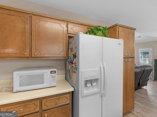 2866 Rosecommons Dr, Hampton, GA 30228 - kitchen with white appliances, light wood-type flooring, light countertops, brown cabinetry, and a textured ceiling