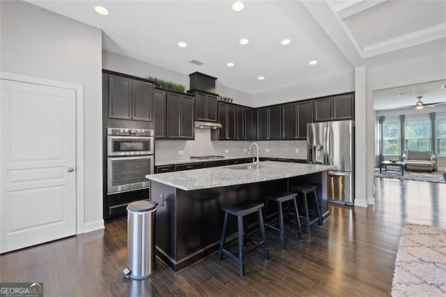 5504 Cameron Parc Dr, Johns Creek, GA 30022 - kitchen featuring appliances with stainless steel finishes, a kitchen island with sink, dark wood-style flooring, light stone counters, and decorative backsplash