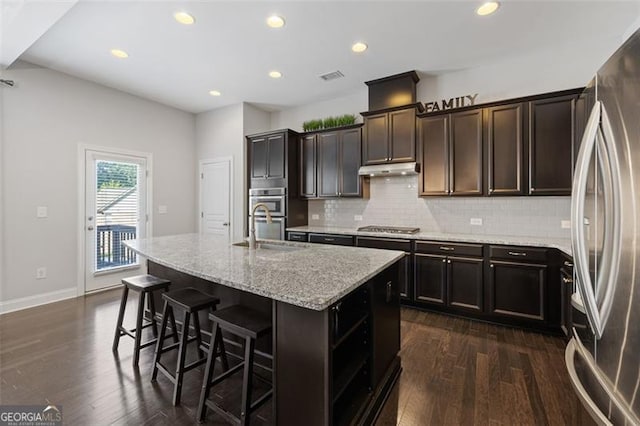 5504 Cameron Parc Dr, Johns Creek, GA 30022 - kitchen with stainless steel appliances, backsplash, dark wood-style flooring, light stone countertops, and a center island with sink