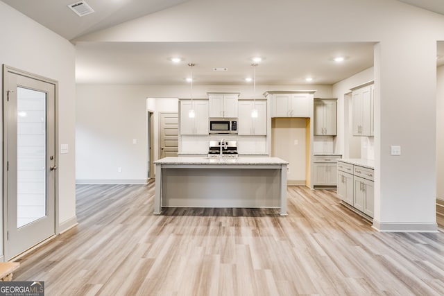 32 Sourwood Dr, Mansfield, GA 30055 - kitchen featuring stainless steel microwave, light wood-style floors, vaulted ceiling, a center island with sink, and light stone countertops