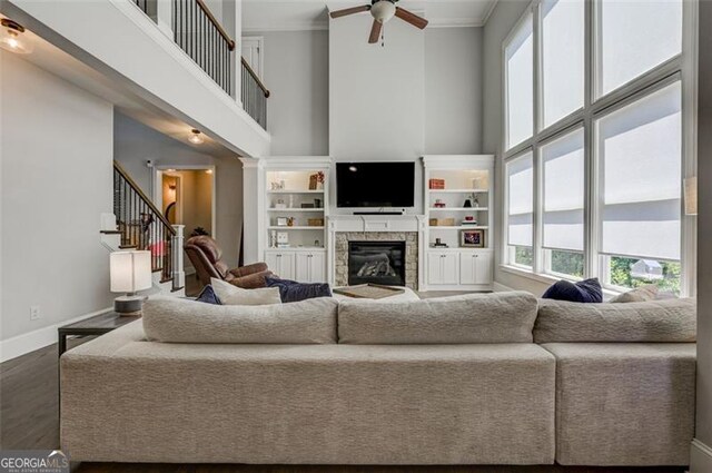 6863 Lake Sterling, Flowery Branch, GA 30542 - living room featuring a high ceiling, a ceiling fan, a stone fireplace, dark wood-type flooring, and ornamental molding