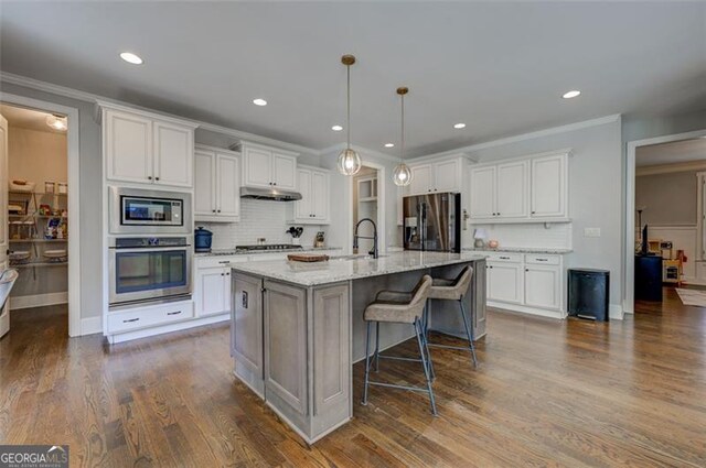 6863 Lake Sterling, Flowery Branch, GA 30542 - kitchen featuring appliances with stainless steel finishes, under cabinet range hood, white cabinets, decorative backsplash, and a breakfast bar area