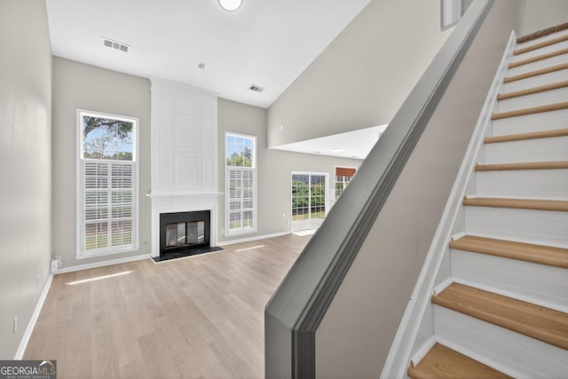 591 Wendlebury Ct, Alpharetta, GA 30004 - unfurnished living room featuring light wood-style flooring, stairs, a large fireplace, and high vaulted ceiling
