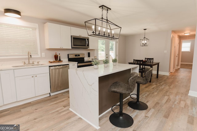 6914 N Baggett Rd, Douglasville, GA 30134 - kitchen with stainless steel appliances, a kitchen island, white cabinets, light wood finished floors, and hanging light fixtures