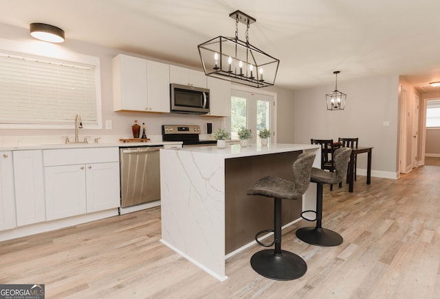 6914 N Baggett Rd, Douglasville, GA 30134 - kitchen featuring stainless steel appliances, light wood-style flooring, a center island, white cabinetry, and hanging light fixtures