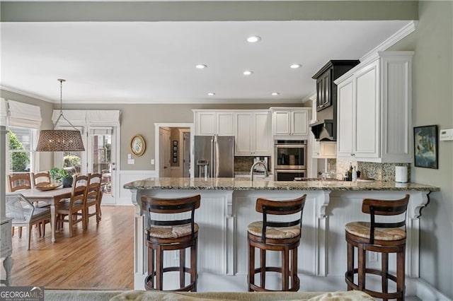 295 Sagamore Cv NW, Sugar Hill, GA 30518 - kitchen featuring stainless steel appliances, ornamental molding, light stone countertops, a peninsula, and a wainscoted wall