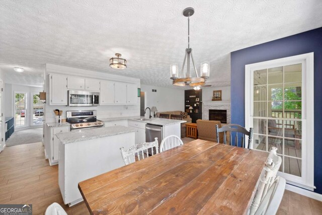 5055 Southland Dr, Woodstock, GA 30188 - dining space featuring a textured ceiling, light wood finished floors, a fireplace, and a chandelier