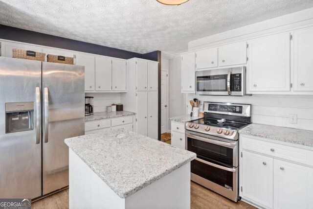 5055 Southland Dr, Woodstock, GA 30188 - kitchen with stainless steel appliances, light wood-type flooring, white cabinets, a center island, and a textured ceiling
