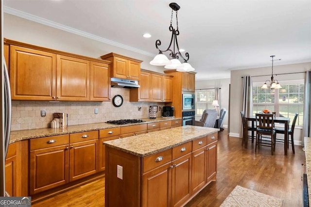 7198 Golfside Dr SE, Covington, GA 30014 - kitchen featuring a chandelier, under cabinet range hood, brown cabinetry, appliances with stainless steel finishes, and backsplash