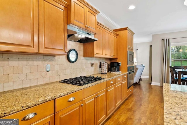 7198 Golfside Dr SE, Covington, GA 30014 - kitchen with under cabinet range hood, stainless steel appliances, light stone counters, backsplash, and wood finished floors