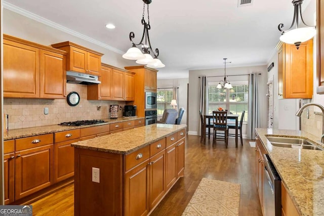7198 Golfside Dr SE, Covington, GA 30014 - kitchen with stainless steel appliances, under cabinet range hood, brown cabinetry, a chandelier, and crown molding