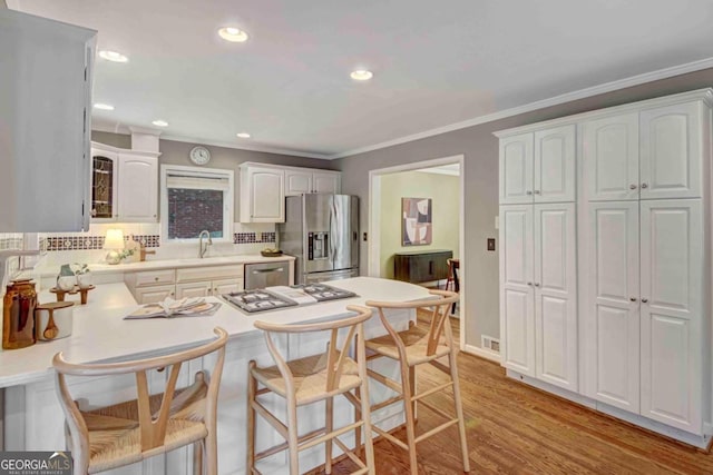 1693 Alderbrook Rd NE, Atlanta, GA 30345 - kitchen with appliances with stainless steel finishes, a peninsula, a kitchen bar, white cabinets, and light wood-style flooring