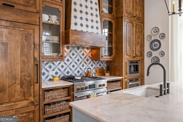 11277 Serenbe Ln, Chattahoochee Hills, GA 30268 - kitchen featuring high end stainless steel range, brown cabinets, decorative backsplash, and glass insert cabinets