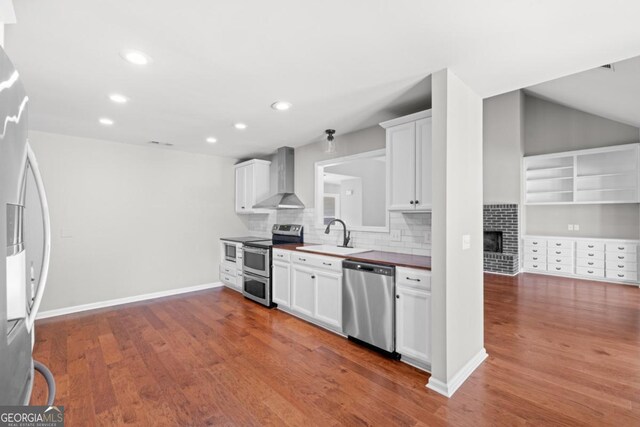 1501 Cayla Way, Statesboro, GA 30458 - kitchen with stainless steel appliances, wall chimney exhaust hood, a fireplace, decorative backsplash, and wood finished floors