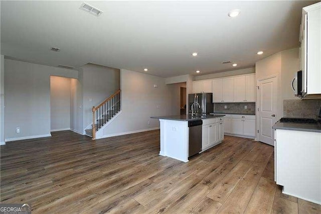 1057 Towne Mill Xing, Canton, GA 30114 - kitchen featuring stainless steel appliances, dark countertops, wood finished floors, white cabinetry, and an island with sink