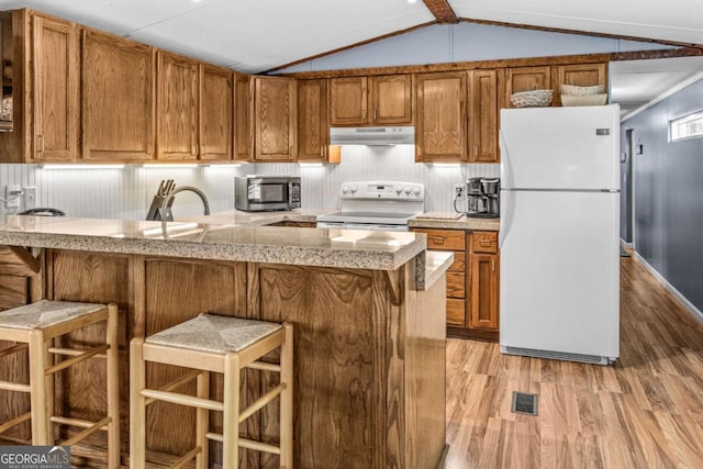 114 Poss Point Cv, Sparta, GA 31087 - kitchen with white appliances, light wood finished floors, under cabinet range hood, brown cabinetry, and vaulted ceiling