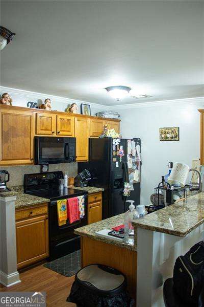 5590 Stonewood Ct, Norcross, GA 30093 - kitchen featuring black appliances, a breakfast bar, ornamental molding, brown cabinetry, and dark wood finished floors