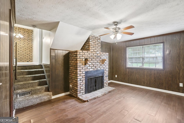 1517 Indian Forest Trl, Stone Mountain, GA 30083 - unfurnished living room with ceiling fan, wood finished floors, wood walls, a brick fireplace, and a textured ceiling