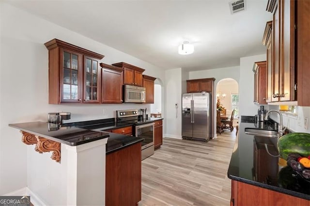 1147 Scenic Park Trl, Lawrenceville, GA 30046 - kitchen featuring appliances with stainless steel finishes, arched walkways, a peninsula, light wood-style flooring, and glass insert cabinets