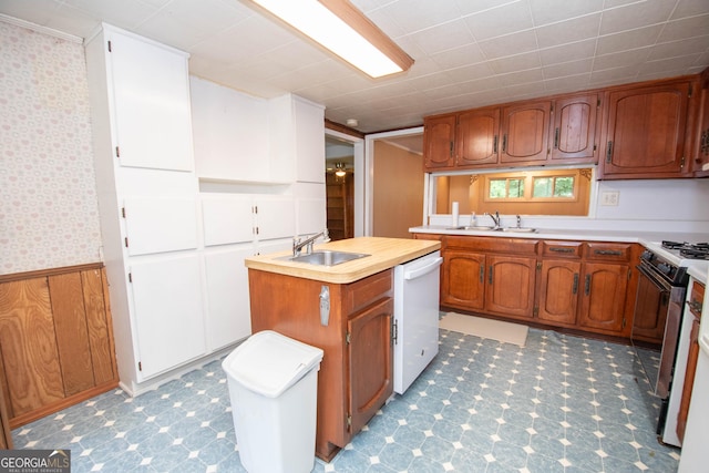 195 Hudgen Rd, Newnan, GA 30265 - kitchen featuring white dishwasher, light countertops, wainscoting, brown cabinetry, and a kitchen island with sink