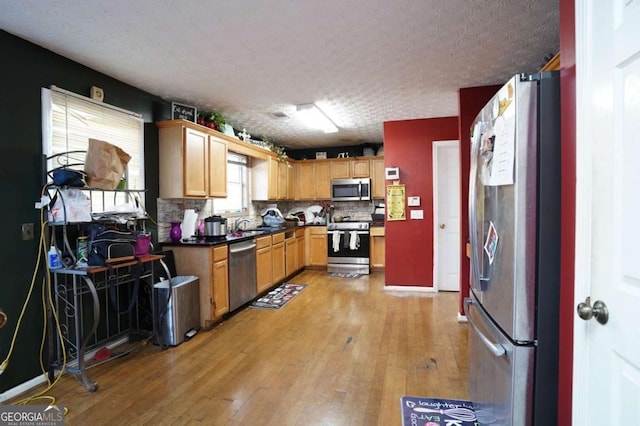 860 Sweet Mill Ln, Lawrenceville, GA 30045 - kitchen featuring stainless steel appliances, light wood finished floors, a textured ceiling, dark countertops, and backsplash