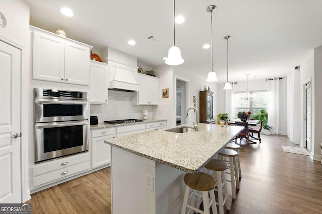 5744 Cypress Bluff Ln, Hoschton, GA 30548 - kitchen with stainless steel double oven, gas stovetop, light wood finished floors, a breakfast bar area, and backsplash