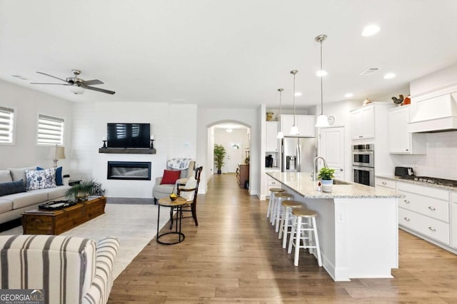 5744 Cypress Bluff Ln, Hoschton, GA 30548 - living area featuring arched walkways, ceiling fan, light wood-style flooring, recessed lighting, and a glass covered fireplace
