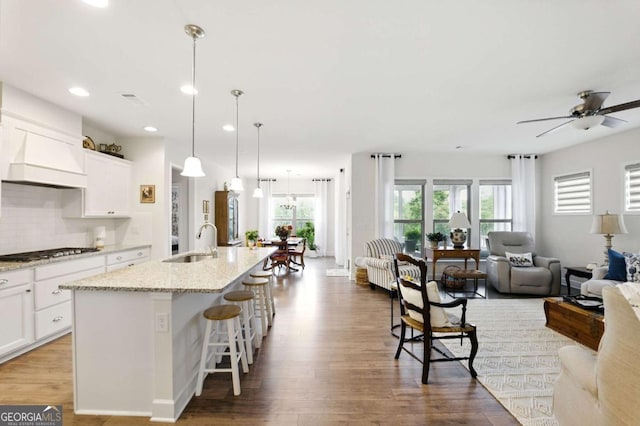 5744 Cypress Bluff Ln, Hoschton, GA 30548 - kitchen with stainless steel gas stovetop, open floor plan, wood finished floors, an island with sink, and ceiling fan