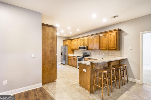 132 Hidden Creek Cir, Lizella, GA 31052 - kitchen featuring appliances with stainless steel finishes, a breakfast bar area, brown cabinets, backsplash, and light countertops