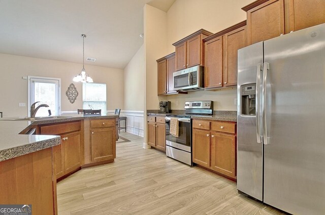 862 Crescent Ln, Griffin, GA 30224 - kitchen with appliances with stainless steel finishes, brown cabinetry, light wood-style flooring, a wainscoted wall, and a chandelier