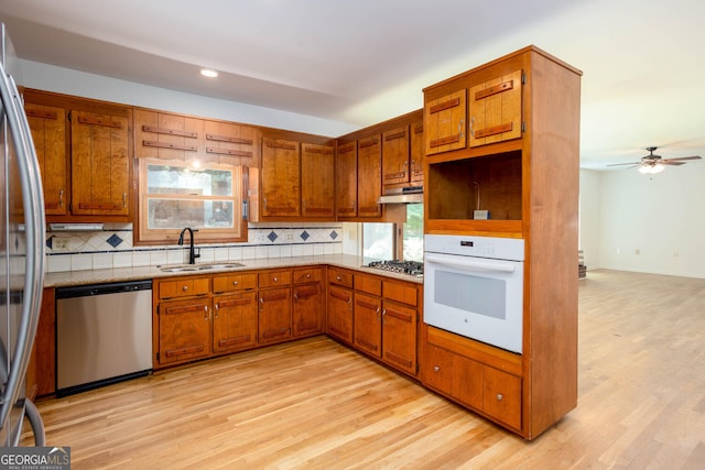 5491 Hiram Rd, Powder Springs, GA 30127 - kitchen featuring appliances with stainless steel finishes, under cabinet range hood, decorative backsplash, brown cabinetry, and light wood-type flooring