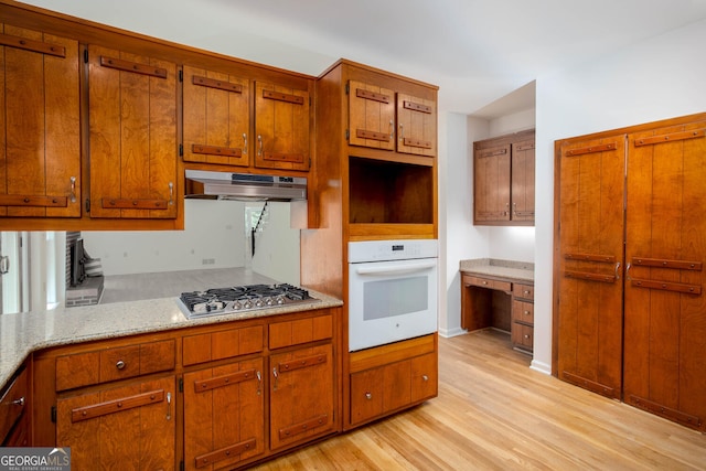 5491 Hiram Rd, Powder Springs, GA 30127 - kitchen featuring oven, under cabinet range hood, stainless steel gas stovetop, light wood finished floors, and brown cabinetry
