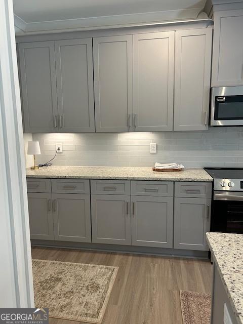 322 Heron St, Ball Ground, GA 30107 - kitchen with appliances with stainless steel finishes, gray cabinetry, light wood-style flooring, tasteful backsplash, and ornamental molding